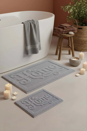 Hellgraues, geprägtes 2-teiliges Bad- und WC-Matten-Set aus Baumwolle mit dem Aufdruck „Home“.