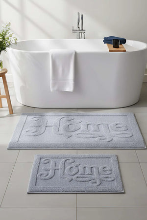 Hellgraues, geprägtes 2-teiliges Bad- und WC-Matten-Set aus Baumwolle mit dem Aufdruck „Home“.